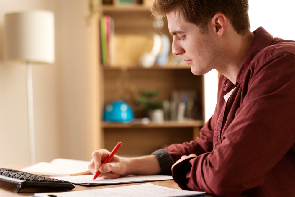 A teenage boy in a red shirt studying at his desk