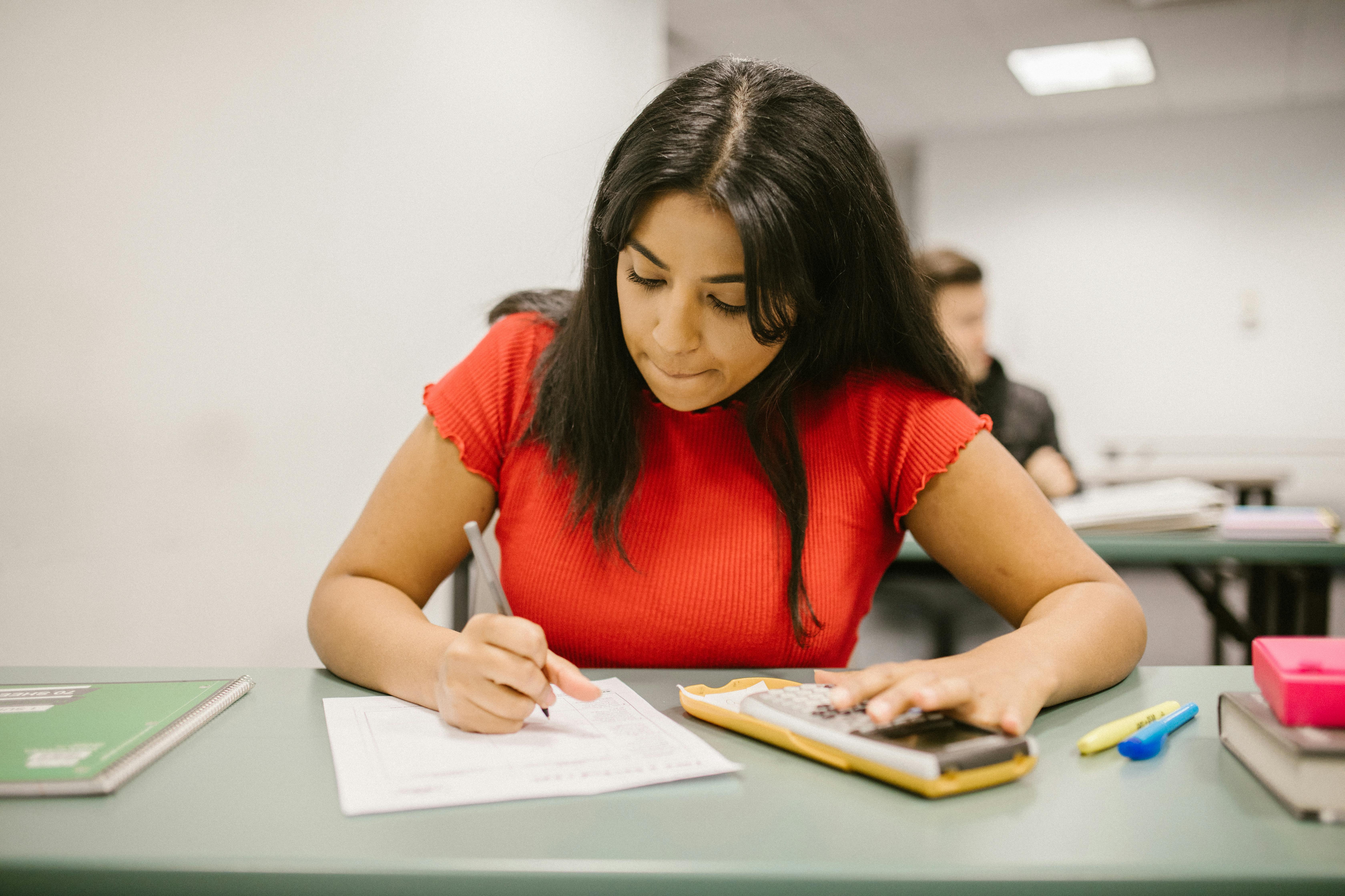Teenage South Asian girl in red using a calculator while taking a maths test