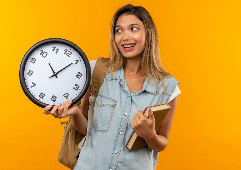 Young female student holding a clock and a book, wearing a backpack