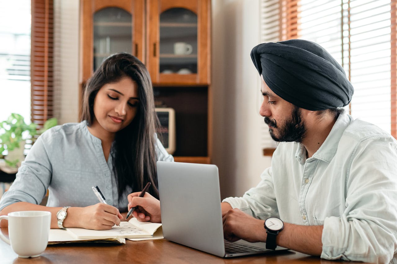 A male Asian tutor tutoring a female Asian sixth form student at her desk