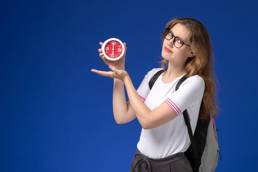 A female teenage student with glasses and a white t-shirt holding a clock